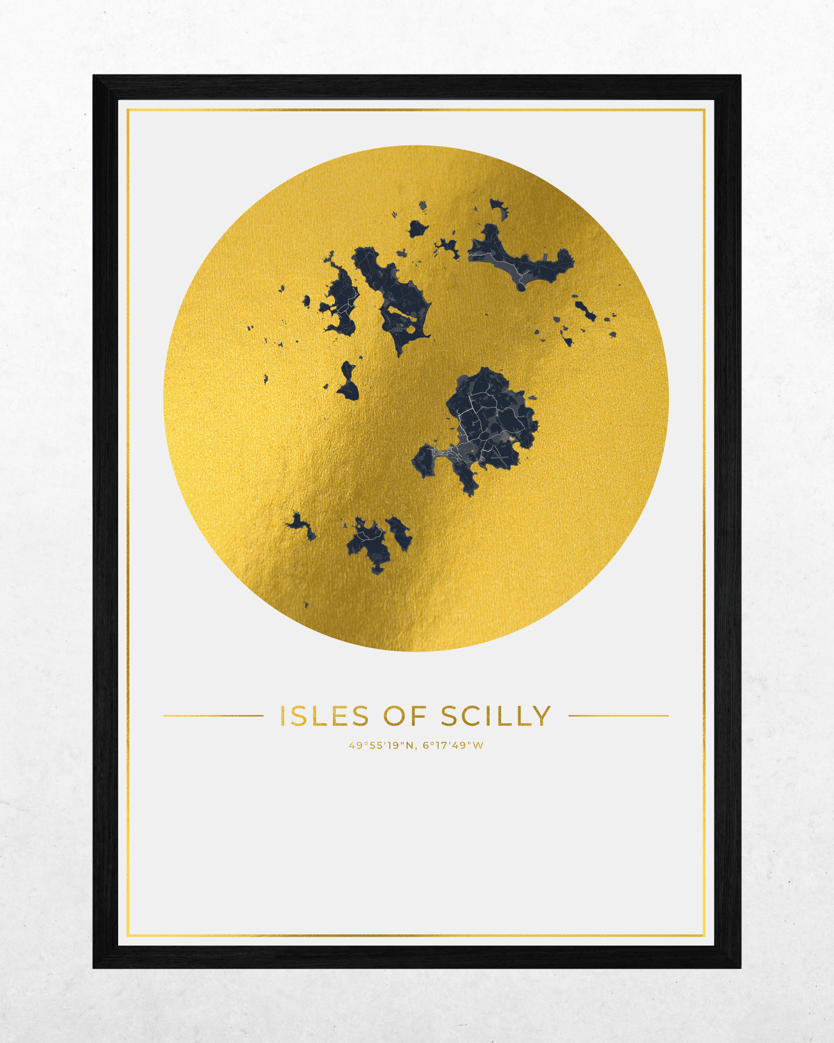 A framed minimalist art print featuring a textured gold circle with a dark blue map of the Isles of Scilly on a white background, with the text 'ISLES OF SCILLY' and coordinates below. The print is framed in a thin white border and a thick black frame, set against a light gray textured wall.