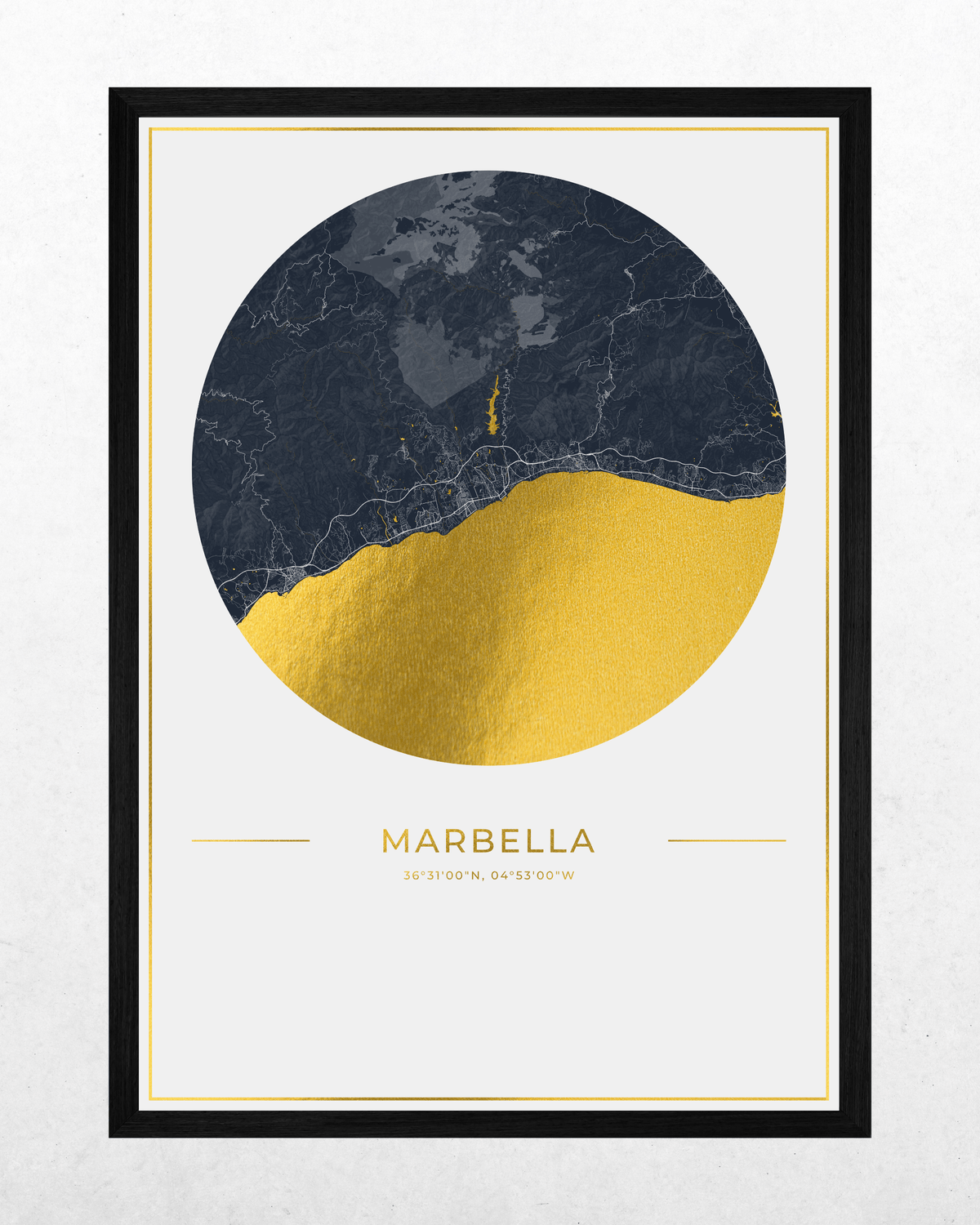 A framed art print featuring a circular map of Marbella, Spain, with a dark navy blue marble texture on the top half and textured gold foil on the bottom half. The print is framed in a black frame with a white mat and gold inner border, set against a light gray textured wall.