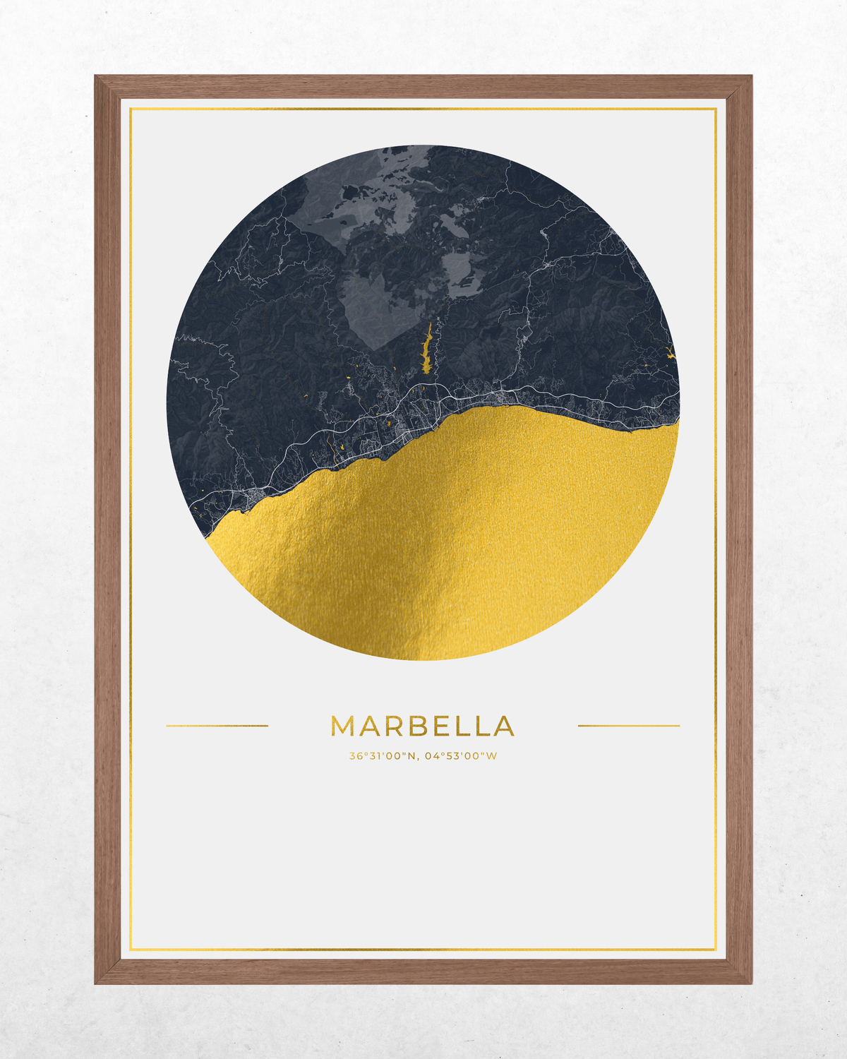 A framed art print featuring a circular map design of Marbella with a dark navy blue top half and a textured gold bottom half, set in a light brown wooden frame against a light gray wall.