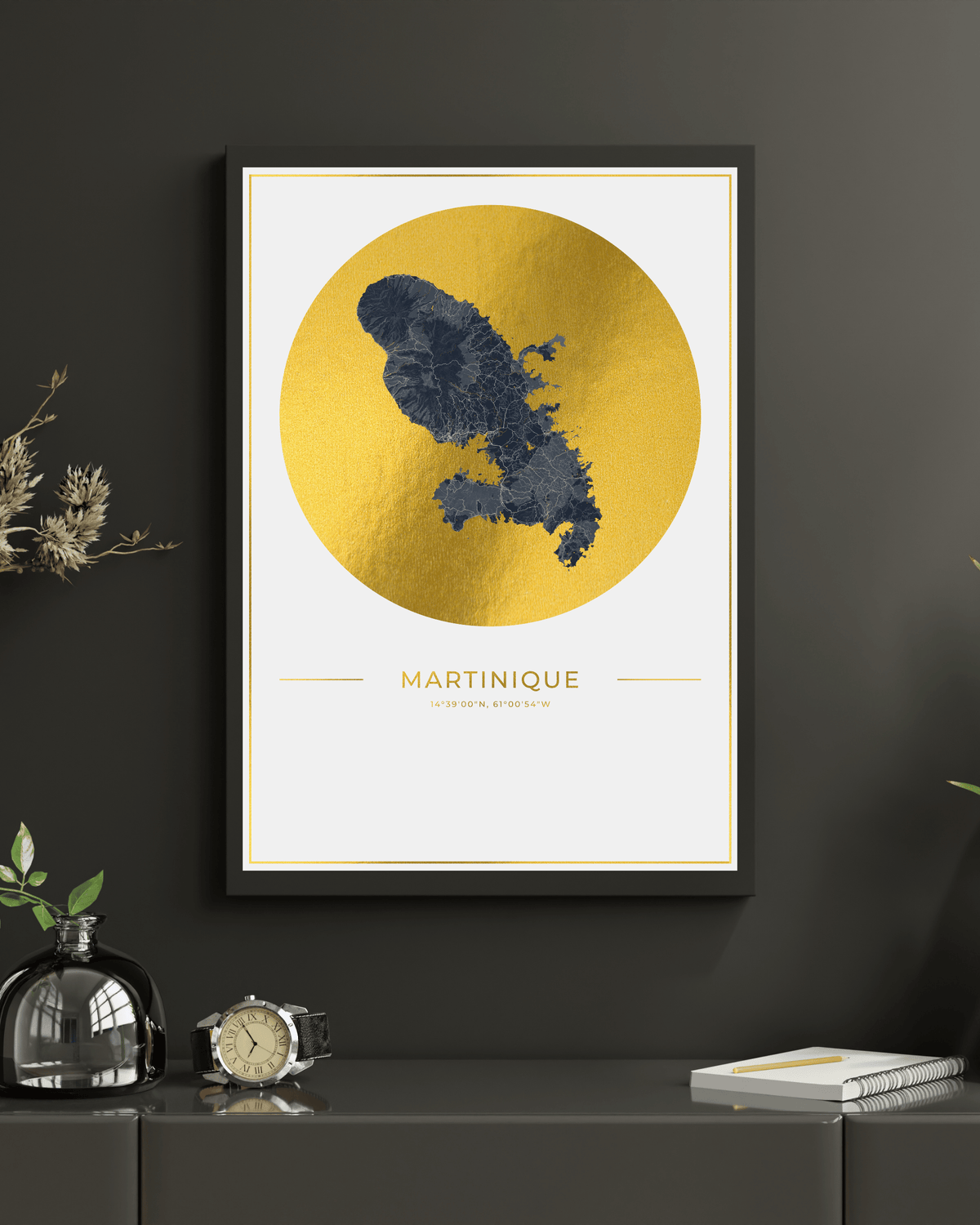 Framed wall art featuring a dark blue map silhouette of Martinique over a large metallic gold circle on a white background, hung on a dark gray wall above a console table with decorative objects.