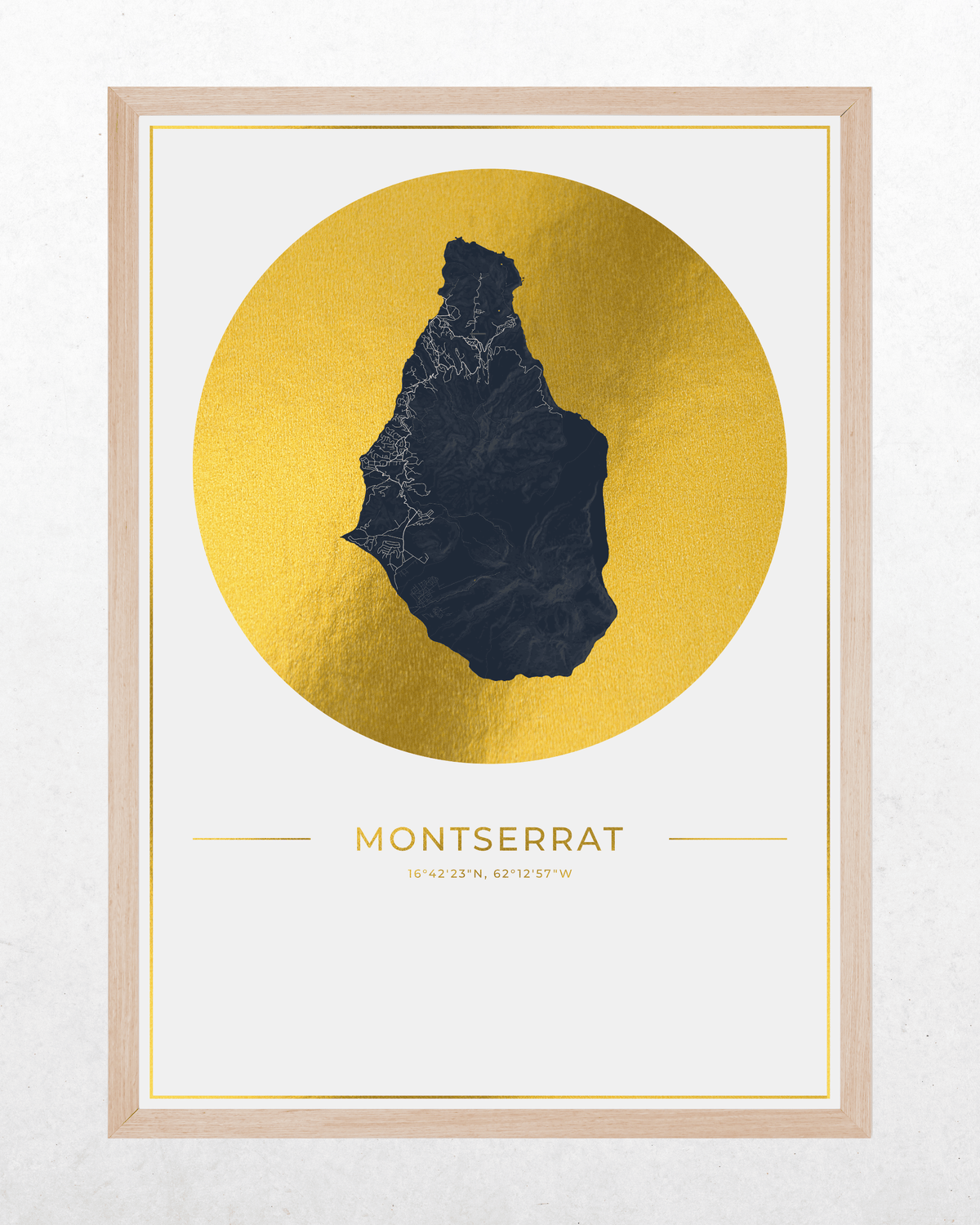A framed minimalist art print featuring a dark navy blue silhouette map of Montserrat overlaid on a large textured gold circle, with the name 'MONTSERRAT' printed below, set in a light wood frame against a white wall.