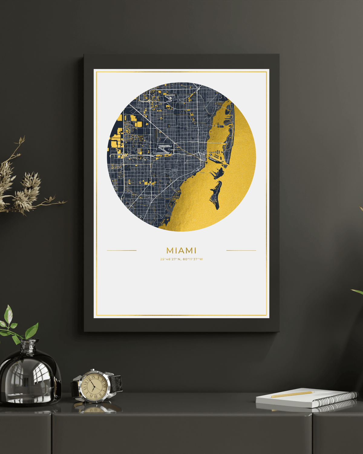 A framed Miami city map art print hangs on a dark gray wall above a console table. The print features a circular map design in navy blue and gold with the text 'MIAMI'