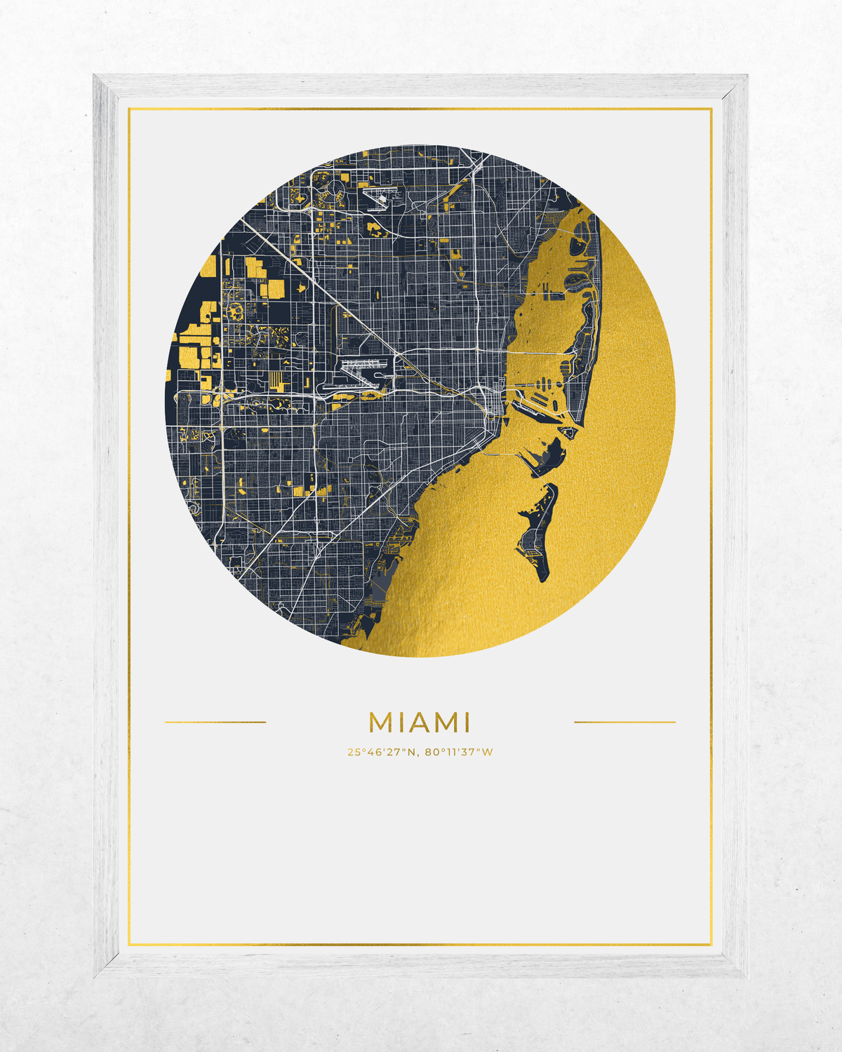 Framed Miami city map wall art print with a white frame, featuring a circular map design in navy blue and metallic gold with the text 'MIAMI' and coordinates below, shown against a light textured background.