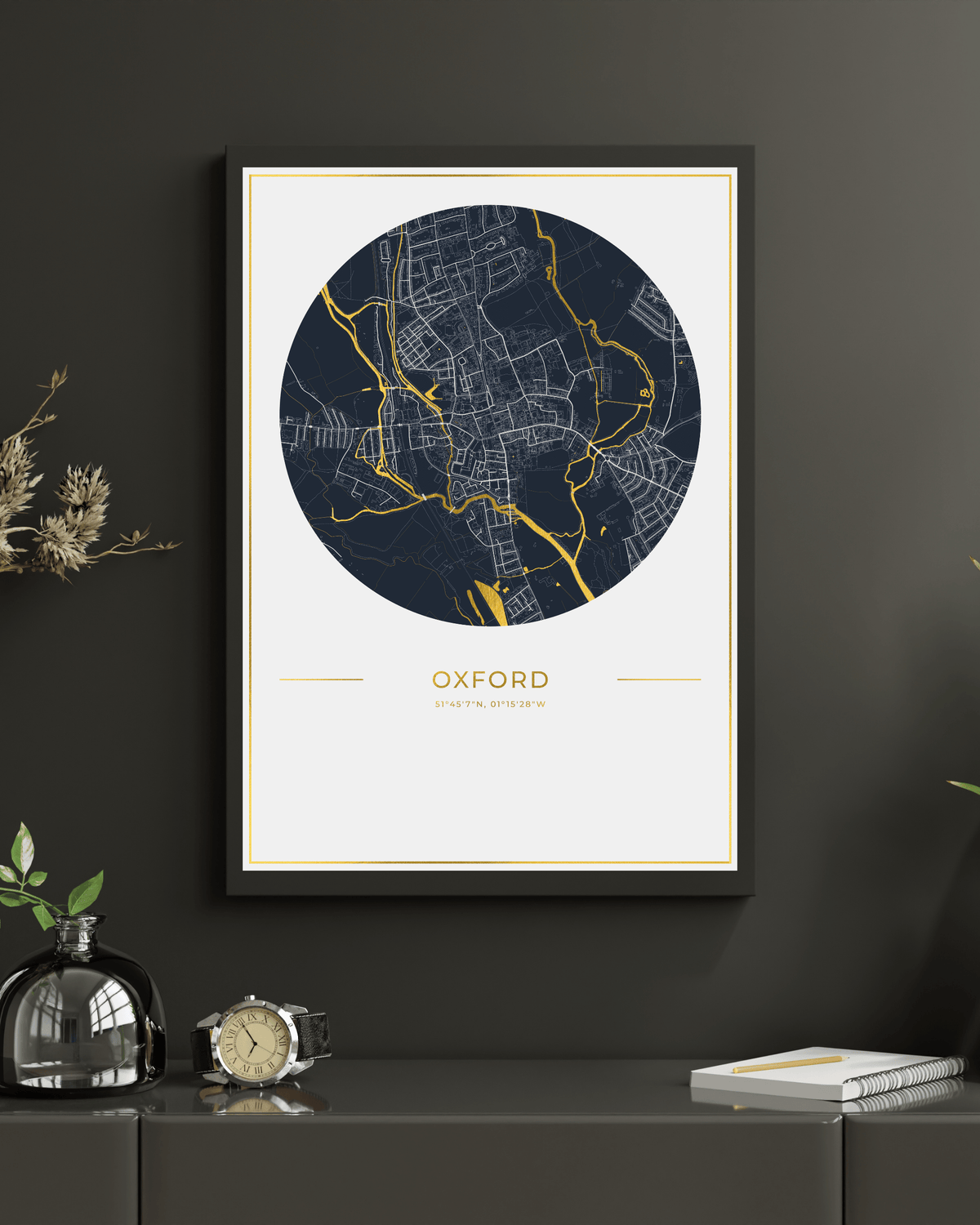 A framed circular map print of Oxford, England, featuring a dark navy blue map with gold street lines on an off-white background, displayed on a dark gray wall above a console table with decorative items.