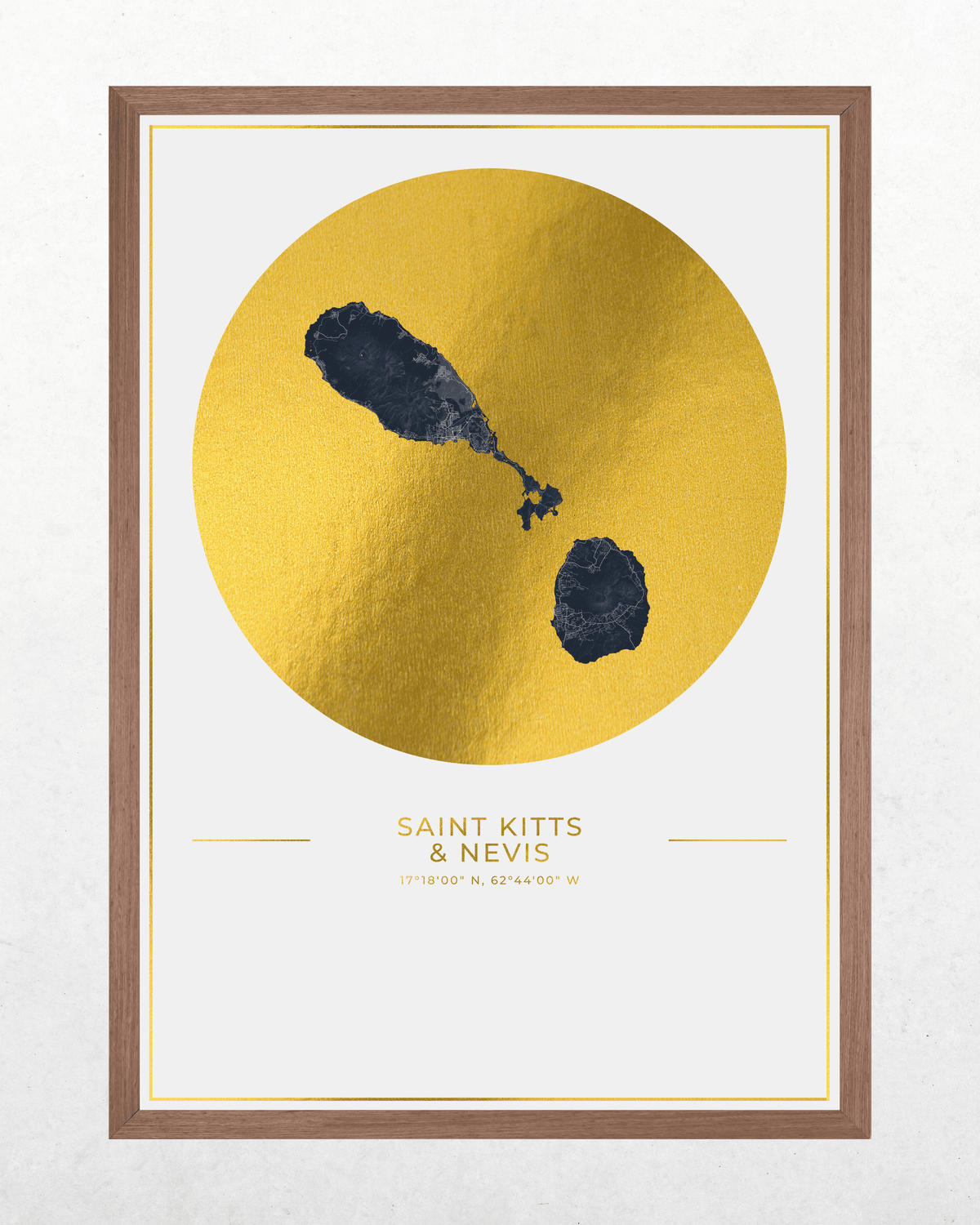 Framed minimalist art print featuring a textured gold circle with two dark blue volcanic landforms on a white background, with the text 'SAINT KITTS & NEVIS' and coordinates below. The print is enclosed in a white mat and a brown wooden frame, set against a light gray textured wall.