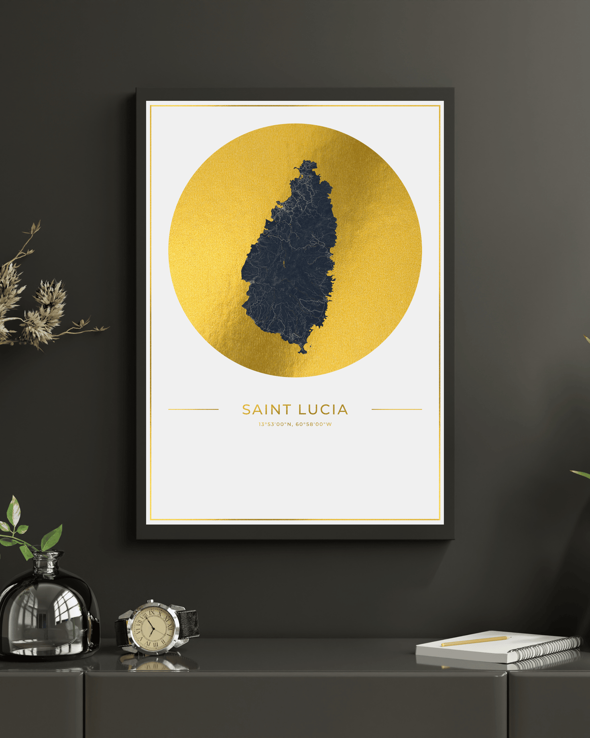 A framed Saint Lucia map art print with a gold circular background and dark blue map silhouette, displayed on a dark gray wall above a console table with decorative objects.