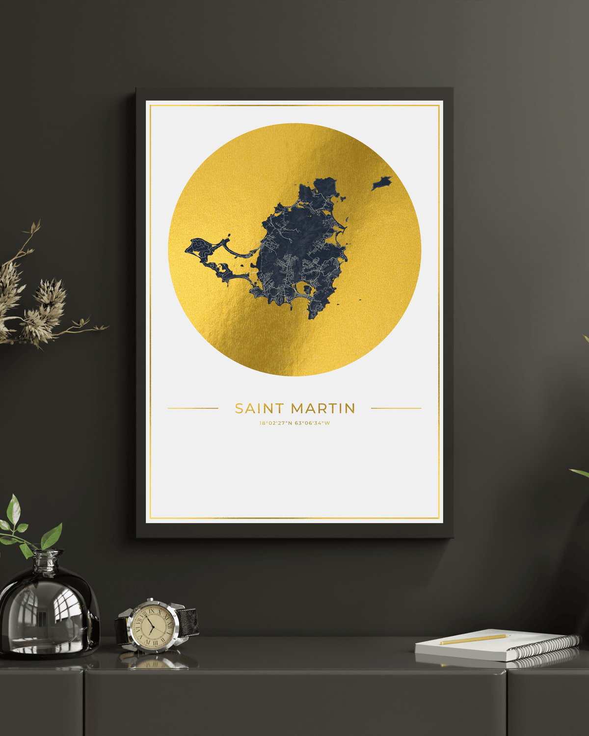 Framed wall art featuring a gold circular map of Saint Martin on a white background, hung on a dark gray wall above a console table with decorative objects.
