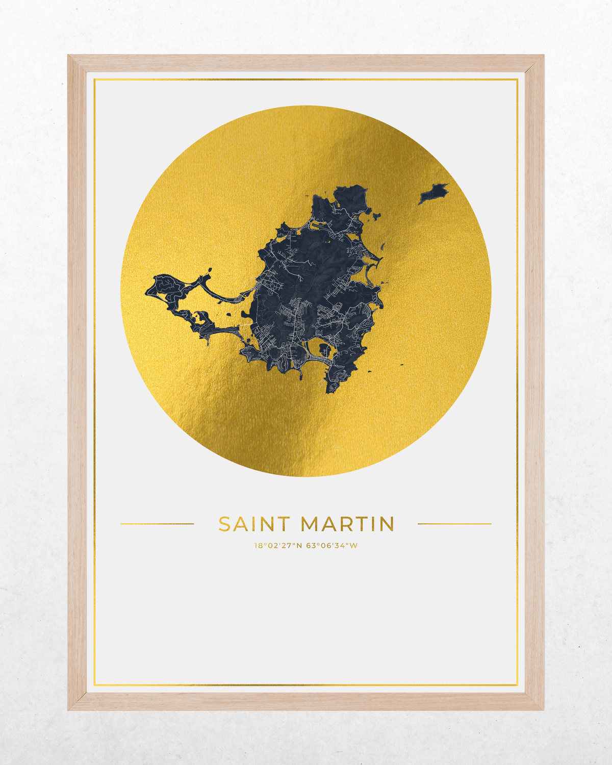 A framed minimalist map print of Saint Martin, featuring a dark blue map silhouette inside a large textured gold circle on a white background, with the text 'SAINT MARTIN' below. The print is housed in a light natural wood frame.