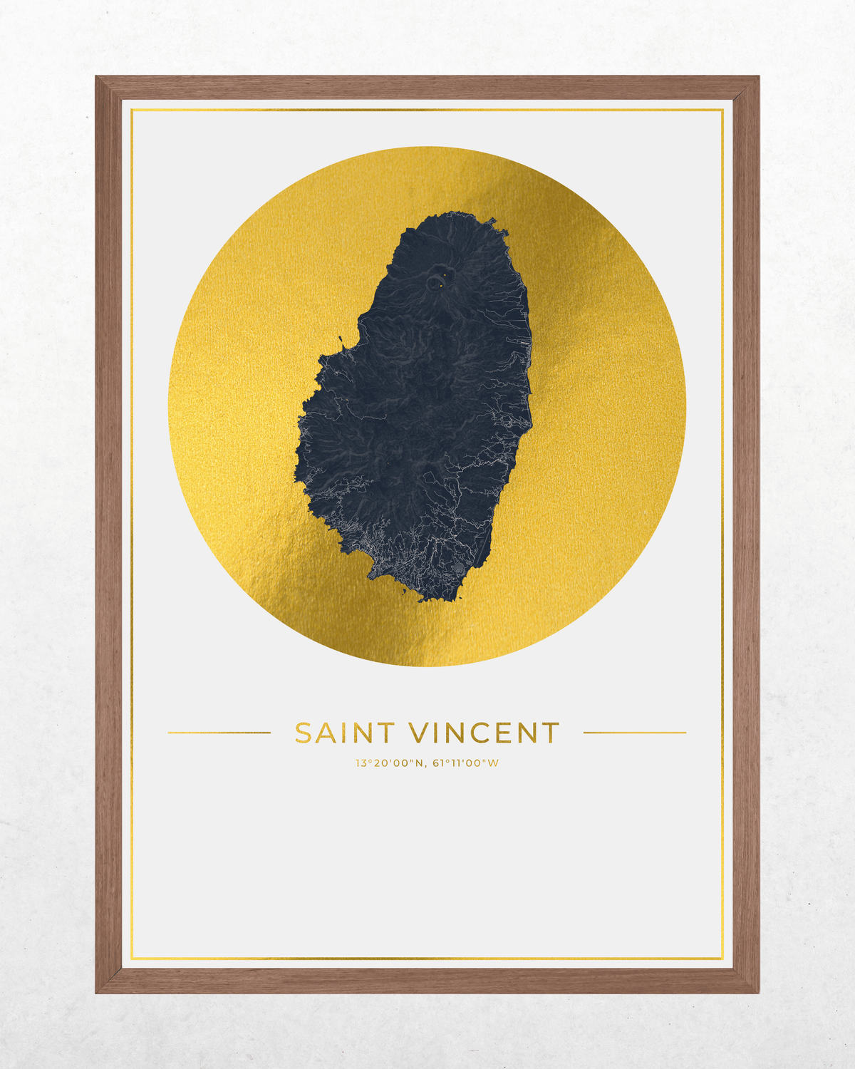 Framed Saint Vincent map art print featuring a dark blue island silhouette centered within a large gold circle on a white background, with the text 'SAINT VINCENT' below. The print is housed in a brown wood frame and shown against a light textured wall.