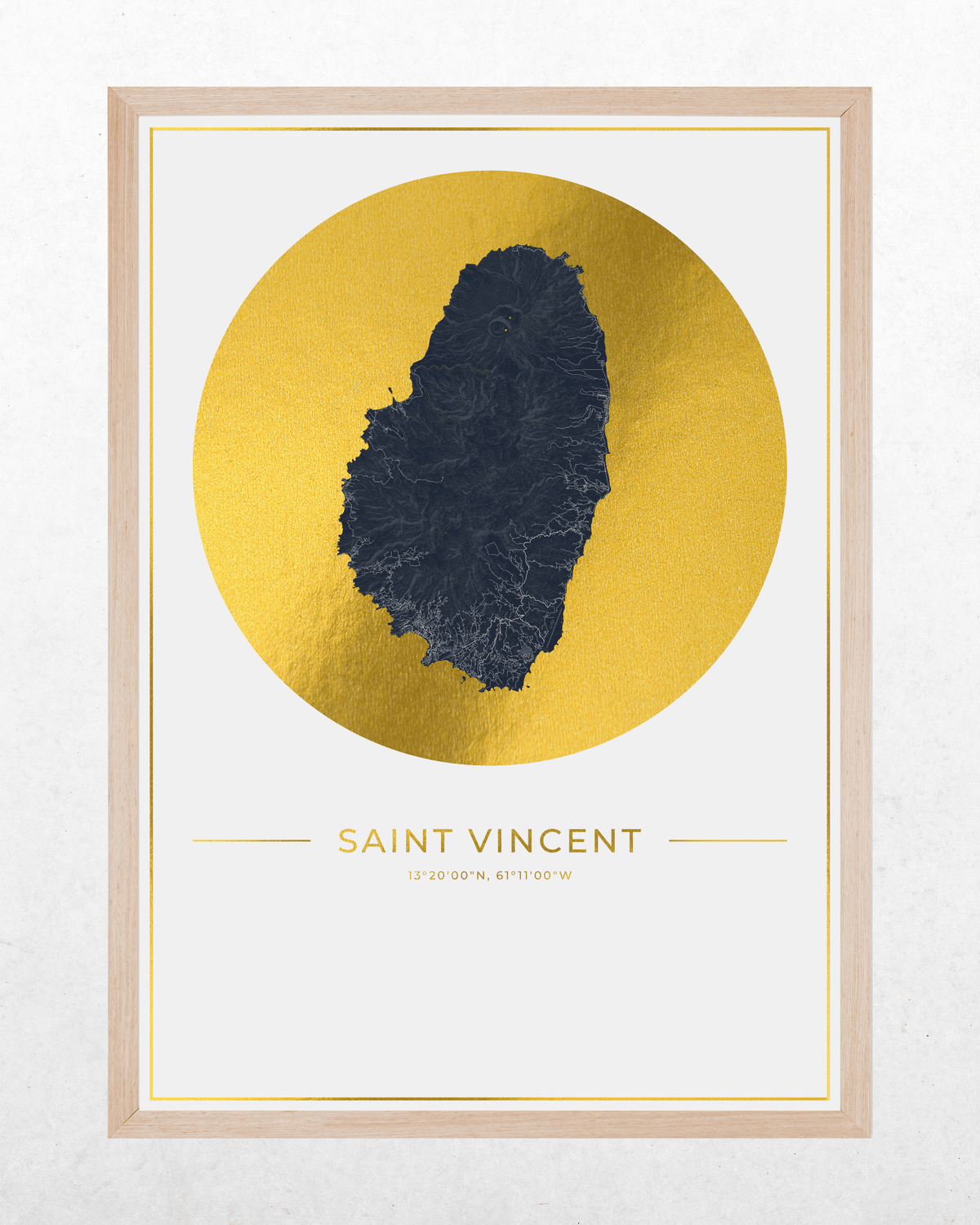Framed wall art print featuring a stylized dark blue map of Saint Vincent centered inside a large metallic gold circle, with the text 'SAINT VINCENT' below. The print is mounted in a light natural wood frame against a light textured wall.