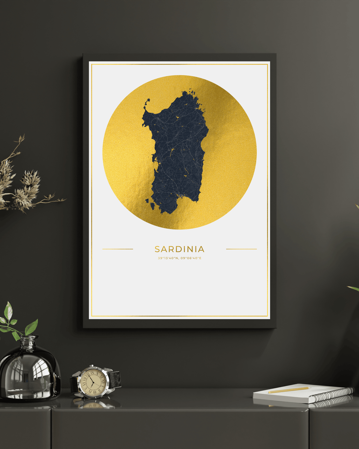 A framed minimalist art print of Sardinia, featuring a dark navy blue map silhouette inside a large textured gold circle on an off-white background, hanging on a dark gray wall above a console table with decorative items.