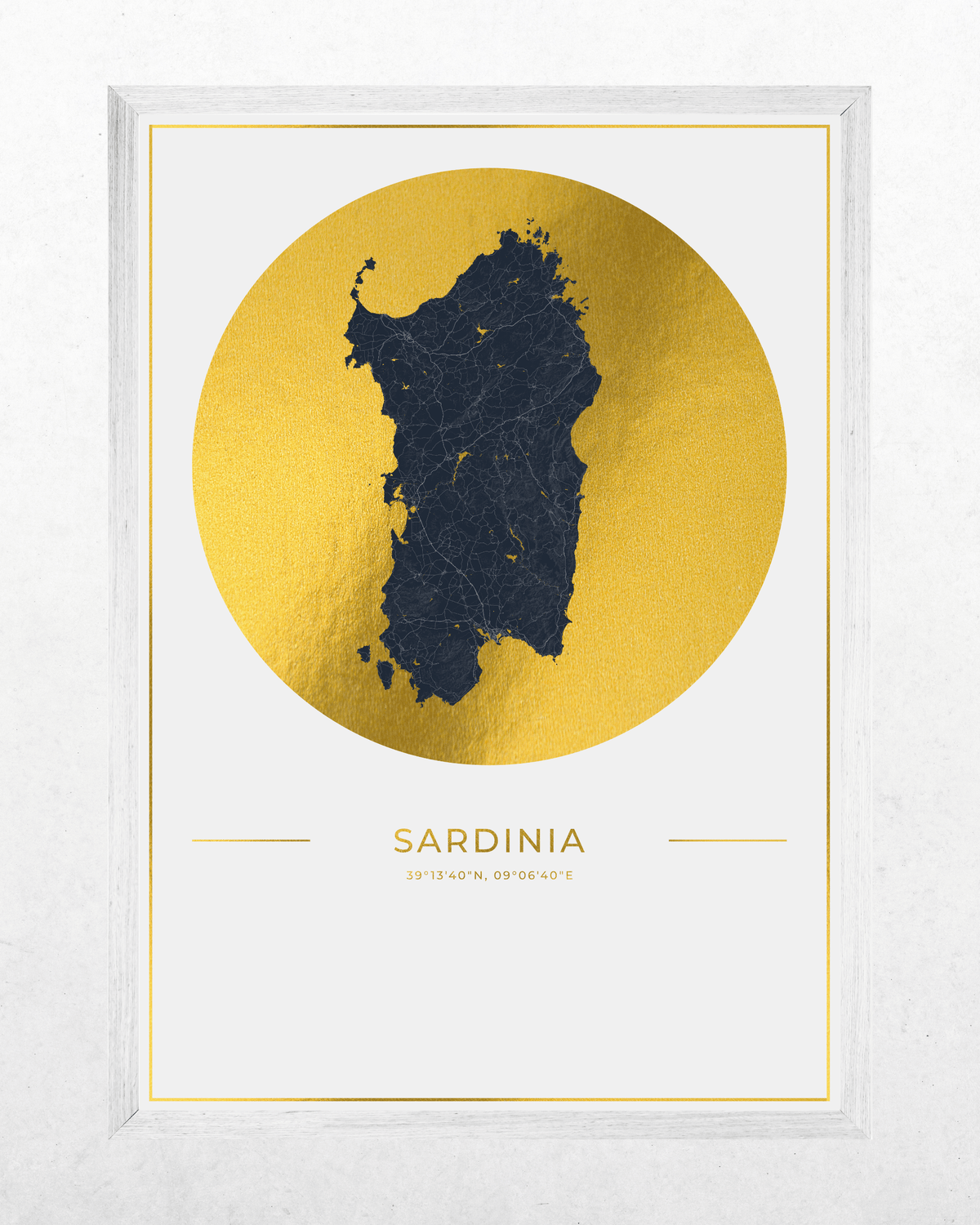 Framed wall art print featuring a dark navy silhouette map of Sardinia centered inside a large metallic gold circle on a white background, with the word SARDINIA and coordinates printed below. The print is housed in a white frame and photographed against a light textured wall.