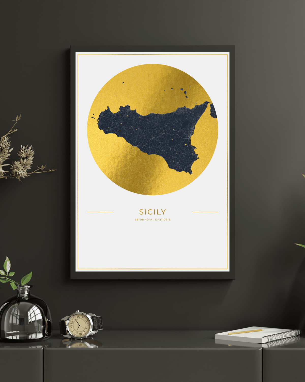 Framed wall art featuring a stylized map of Sicily in dark navy blue inside a large textured gold circle, displayed on a dark gray wall above a console table with decorative objects.