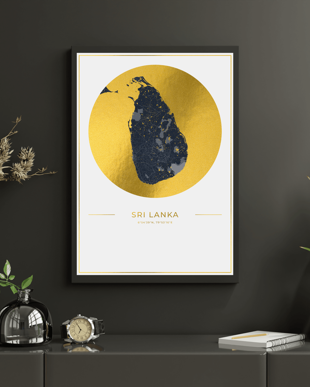 Framed wall art featuring a stylized map of Sri Lanka in dark navy blue over a large metallic gold circle, displayed on a dark gray wall above a console table with decorative objects.