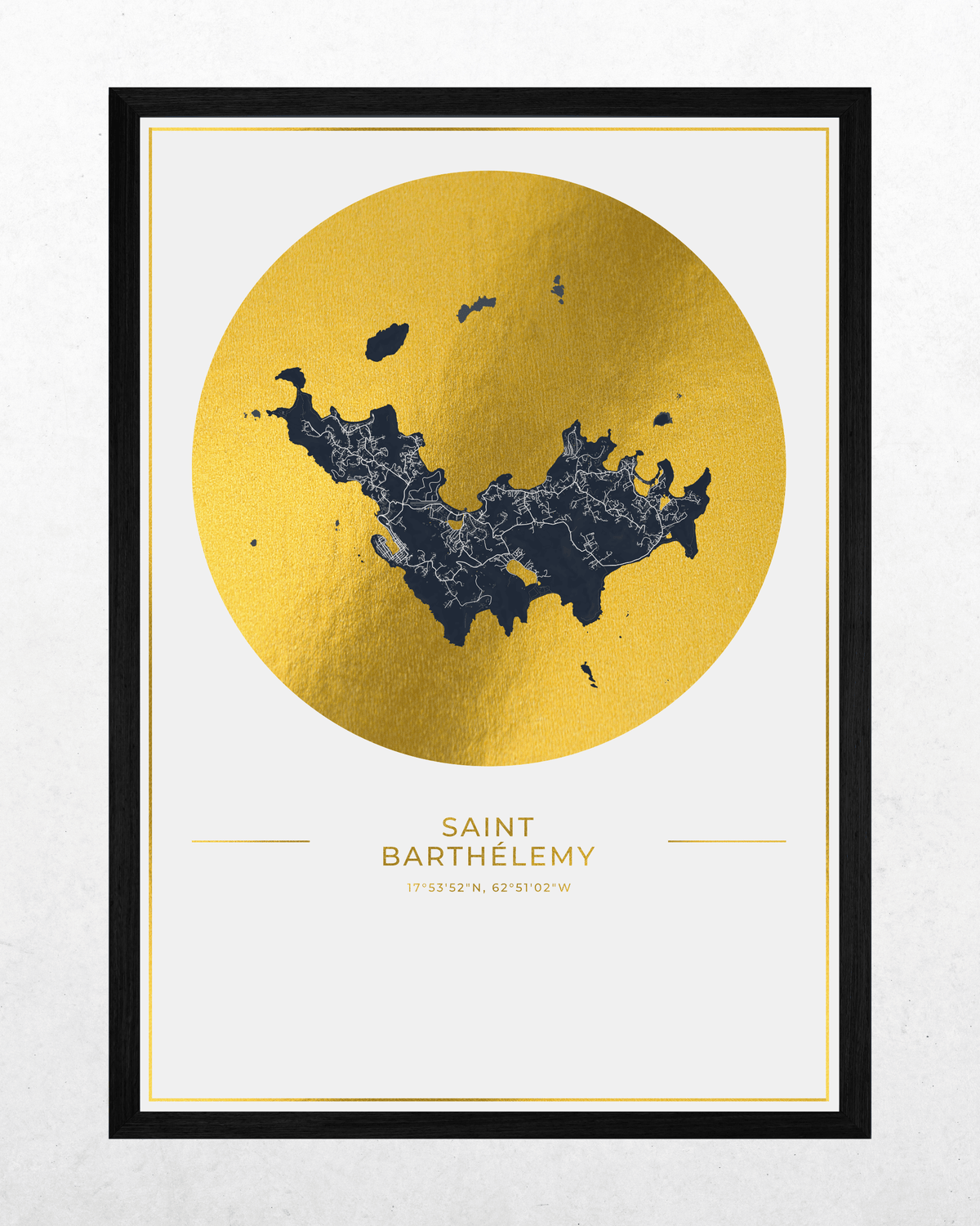 A framed art print featuring a gold foil map of Saint Barthelmy, with a dark navy blue city silhouette overlaid inside a large gold circle. The print is titled 'SAINT BARTHEMY' with coordinates below, set in a black frame against a light textured background.