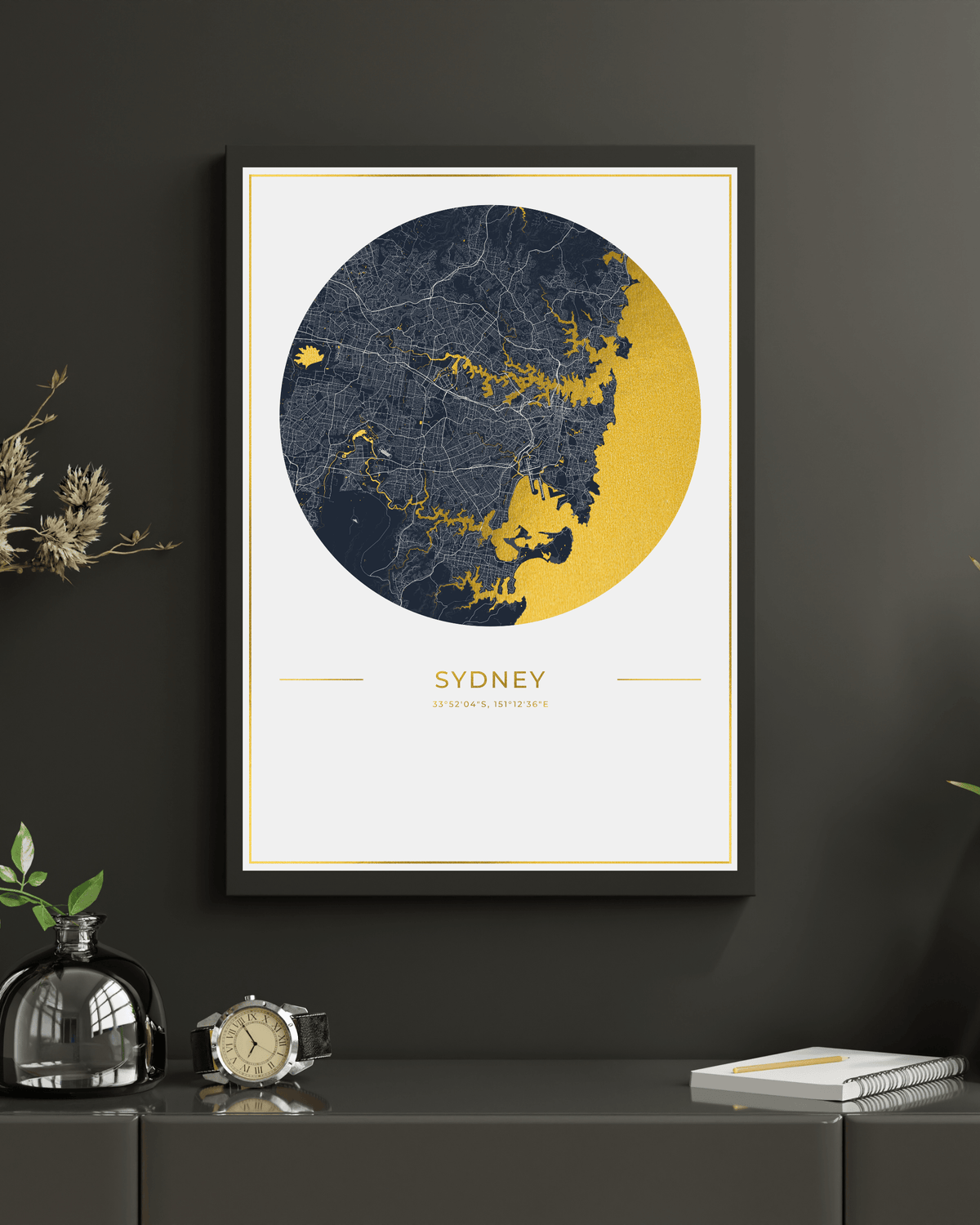 A framed Sydney city map art print hangs on a dark charcoal wall above a console table. The print features a circular map design in navy blue and mustard yellow on a white background, with the text 'SYDNEY' 