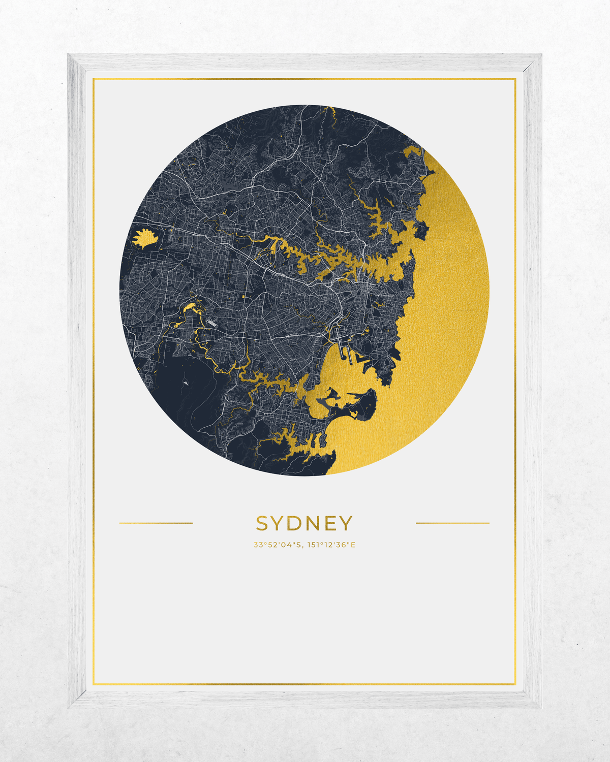 Framed Sydney city map art print with a circular navy and gold map design, gold text reading 'SYDNEY' , shown in a white frame against a light textured wall.
