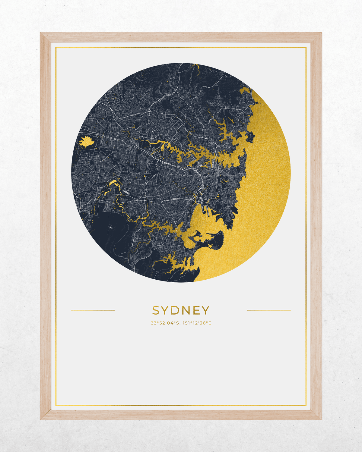 A framed Sydney map art print featuring a circular graphic with a dark navy street map and gold coastline details, set within a light wood frame on a textured off-white background.