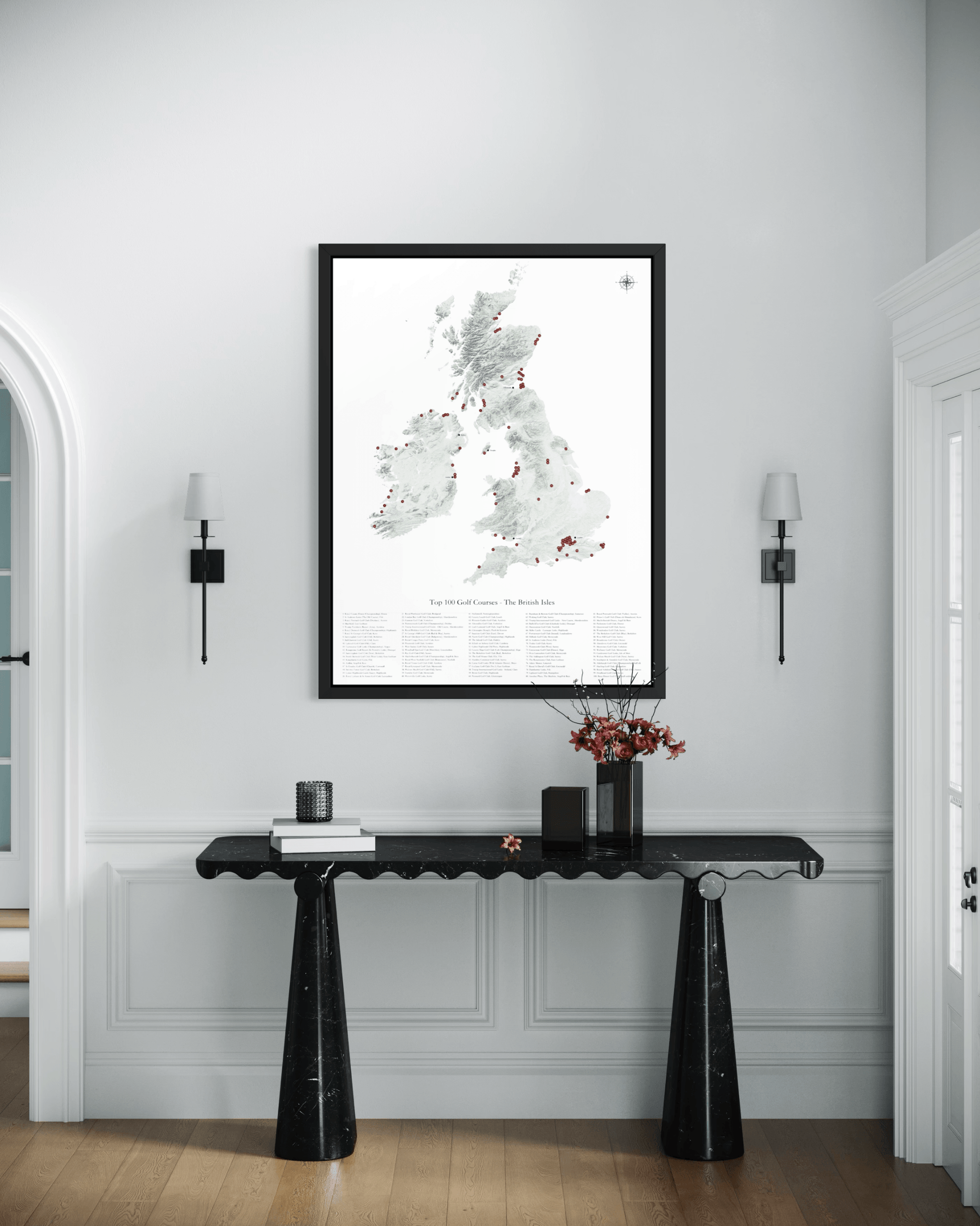 A framed art print of a map of Great Britain and Ireland hangs on a white wall above a black console table in a styled interior room.