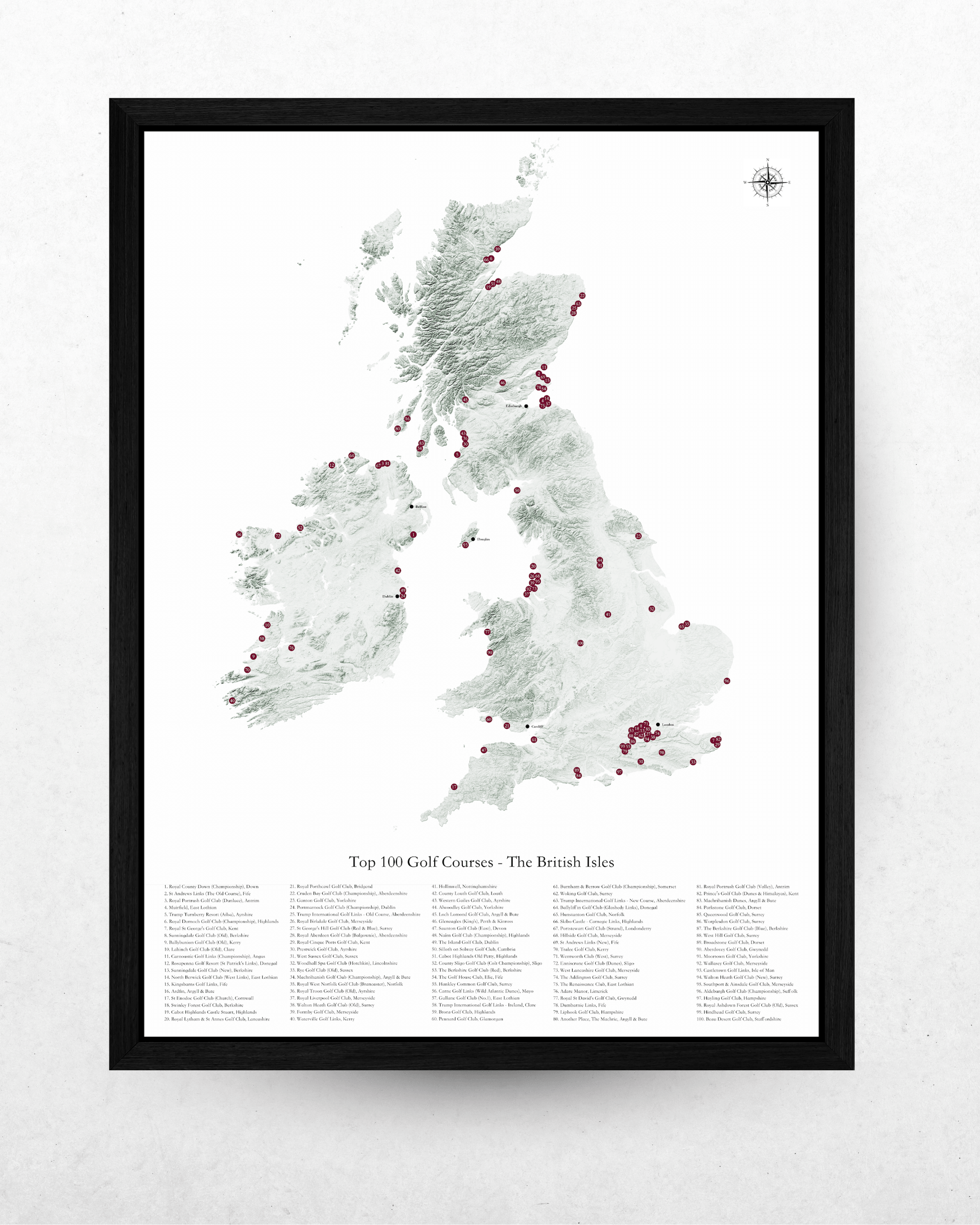 A framed vertical map print of the British Isles showing the top 100 golf courses, with a black frame on a light textured wall.