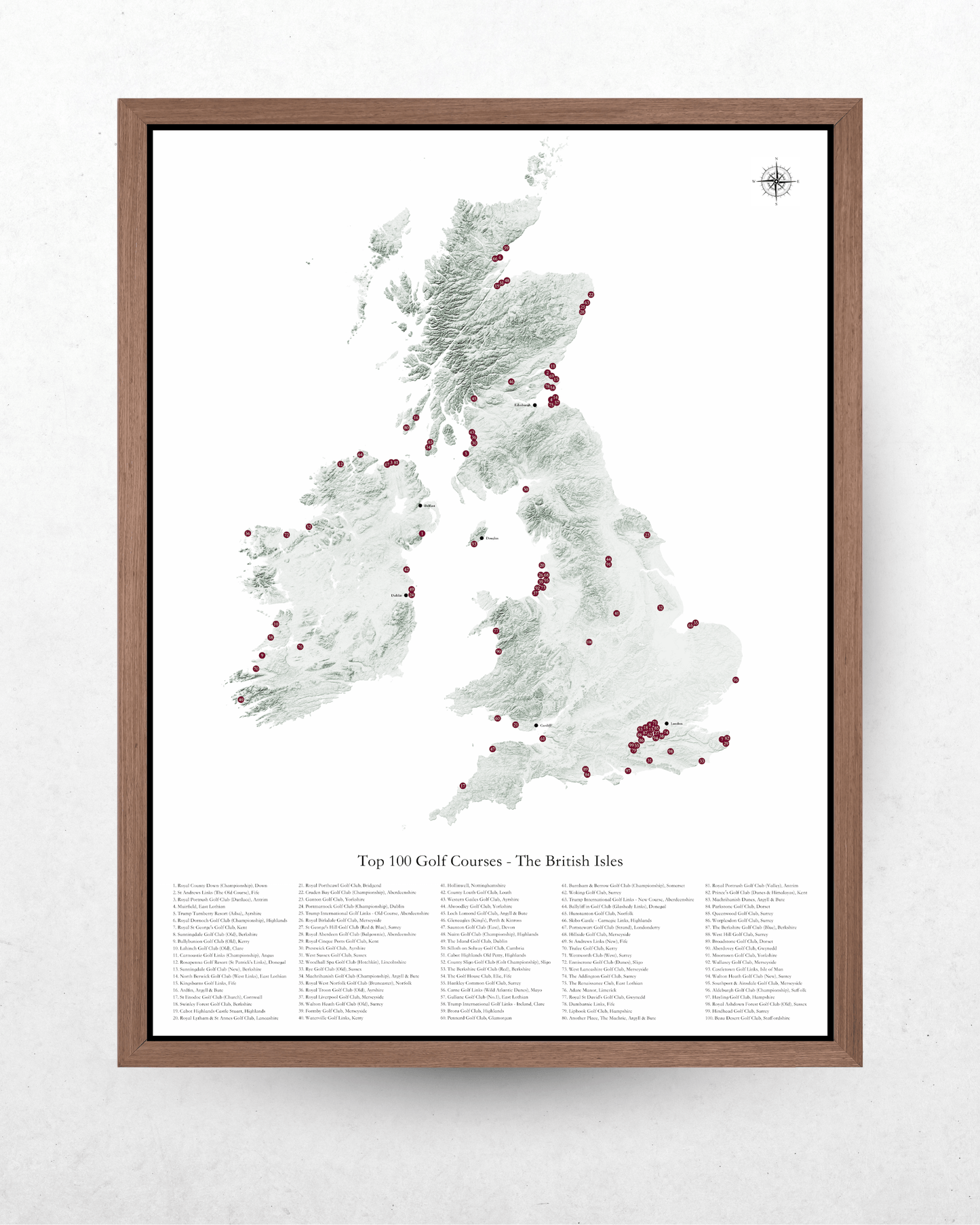 A framed map print of the United Kingdom highlighting the 'Top 300 Golf Courses - The British Isles' with a dark brown wood frame, displayed on a textured white wall.