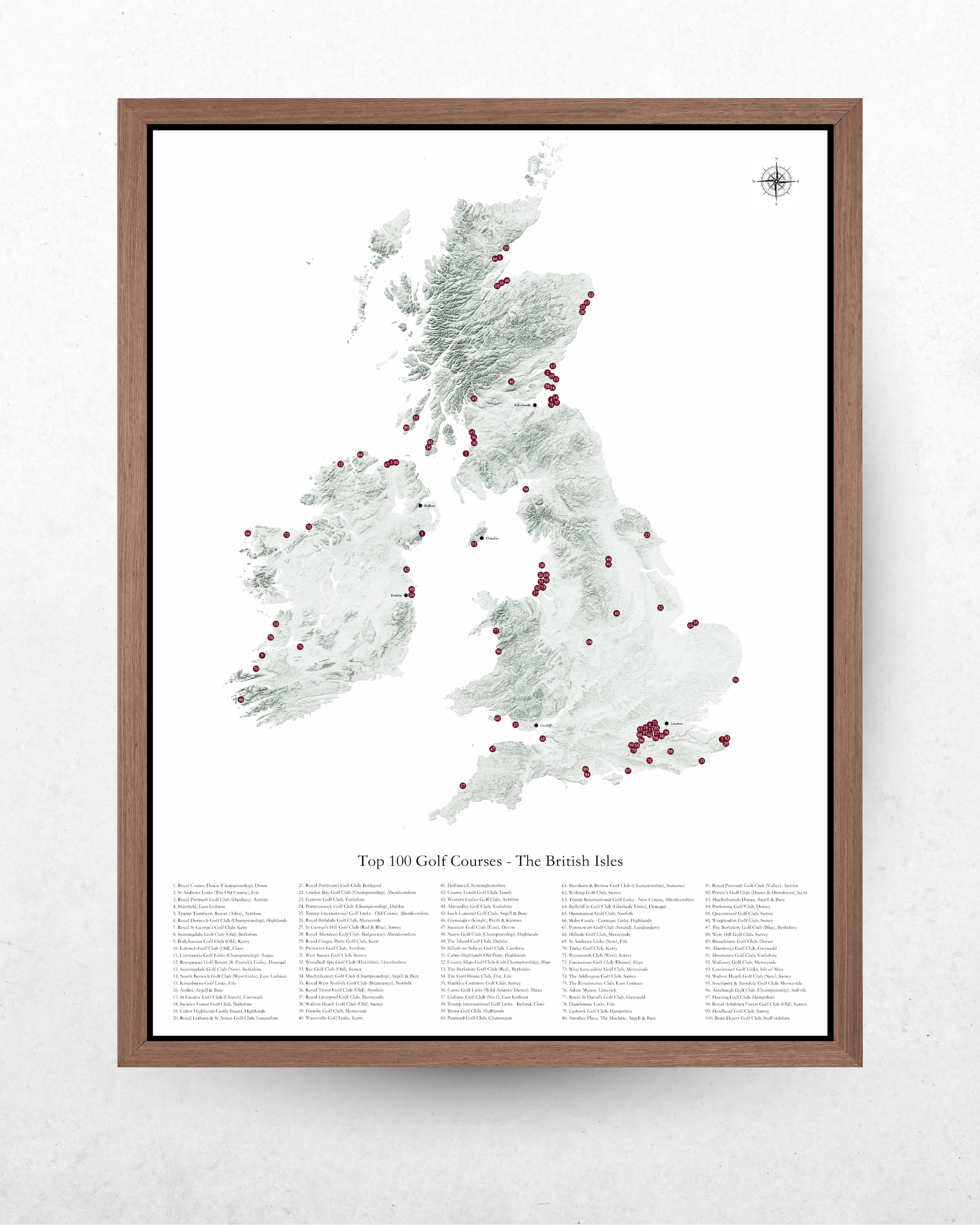 A framed map print of the United Kingdom highlighting the 'Top 300 Golf Courses - The British Isles' with a dark brown wood frame, displayed on a textured white wall.