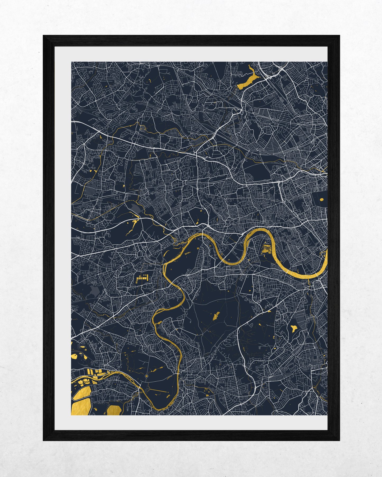 A framed city map print of London, featuring a dark navy blue background with white street lines and the River Thames highlighted in gold. The print is matted with a white border and enclosed in a slim black frame, set against a light gray textured wall.
